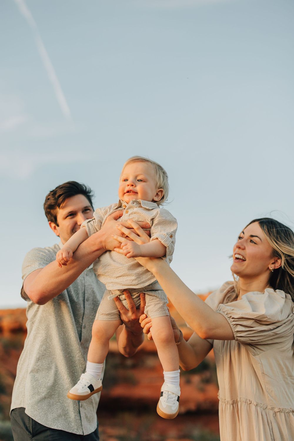 A happy family playing together outdoors, with a smiling baby being held by the parents.