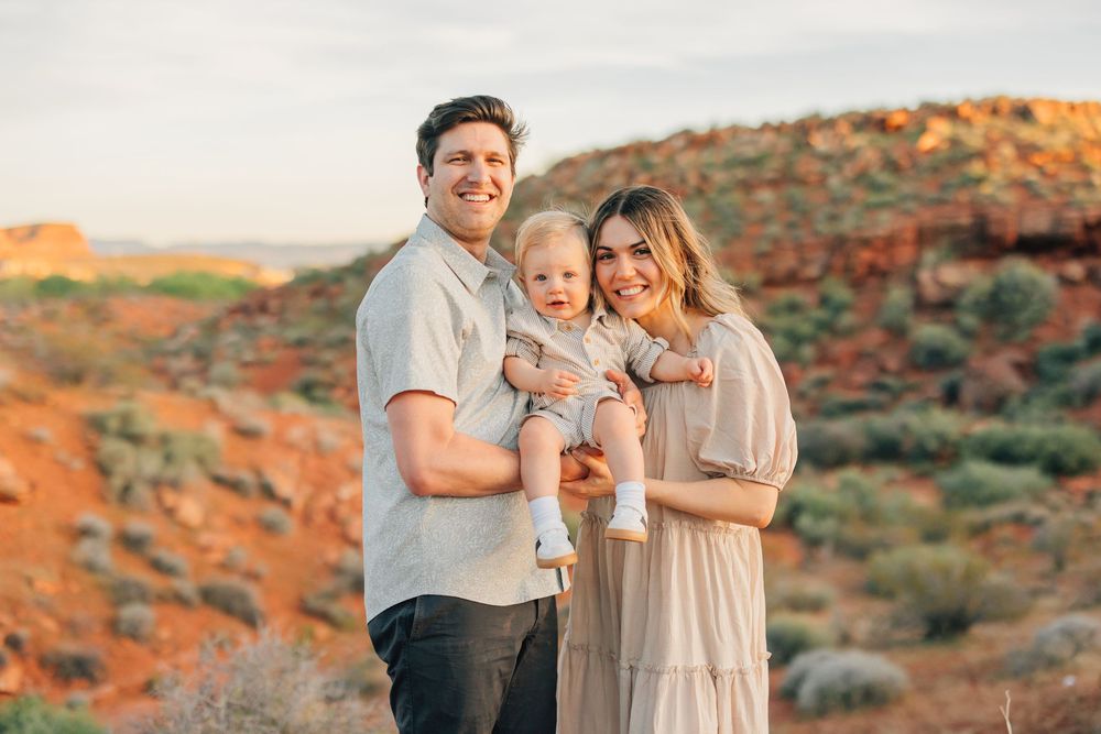 A happy family of three posing together in a scenic desert landscape with vibrant orange rocks.
