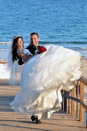 The groom carries the bride in his arms along the beach in the Algarve.