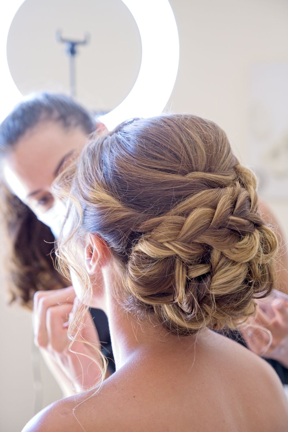 Bride getting her makeup done, seen from behind.