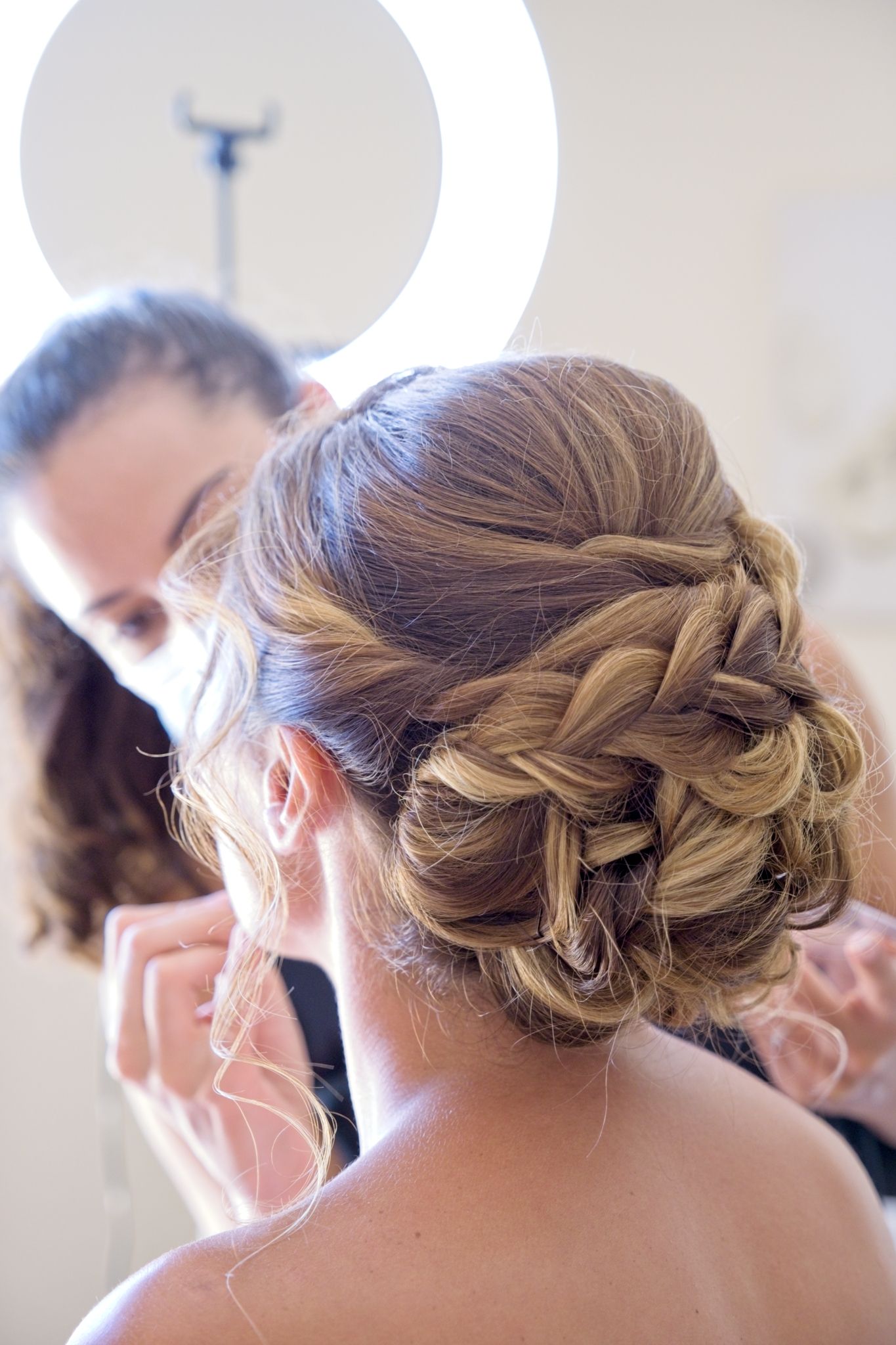 Bride getting her makeup done, seen from behind.