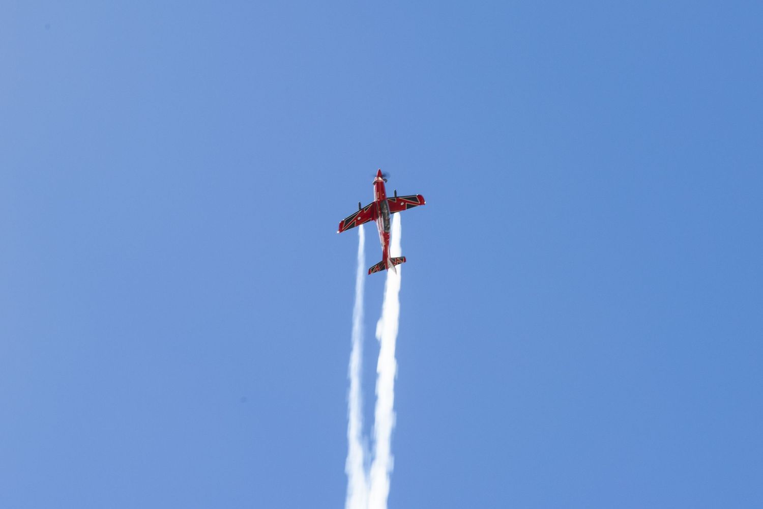 White smoke trails streak across a bright blue sky as jets perform an aerial maneuver during an airshow.