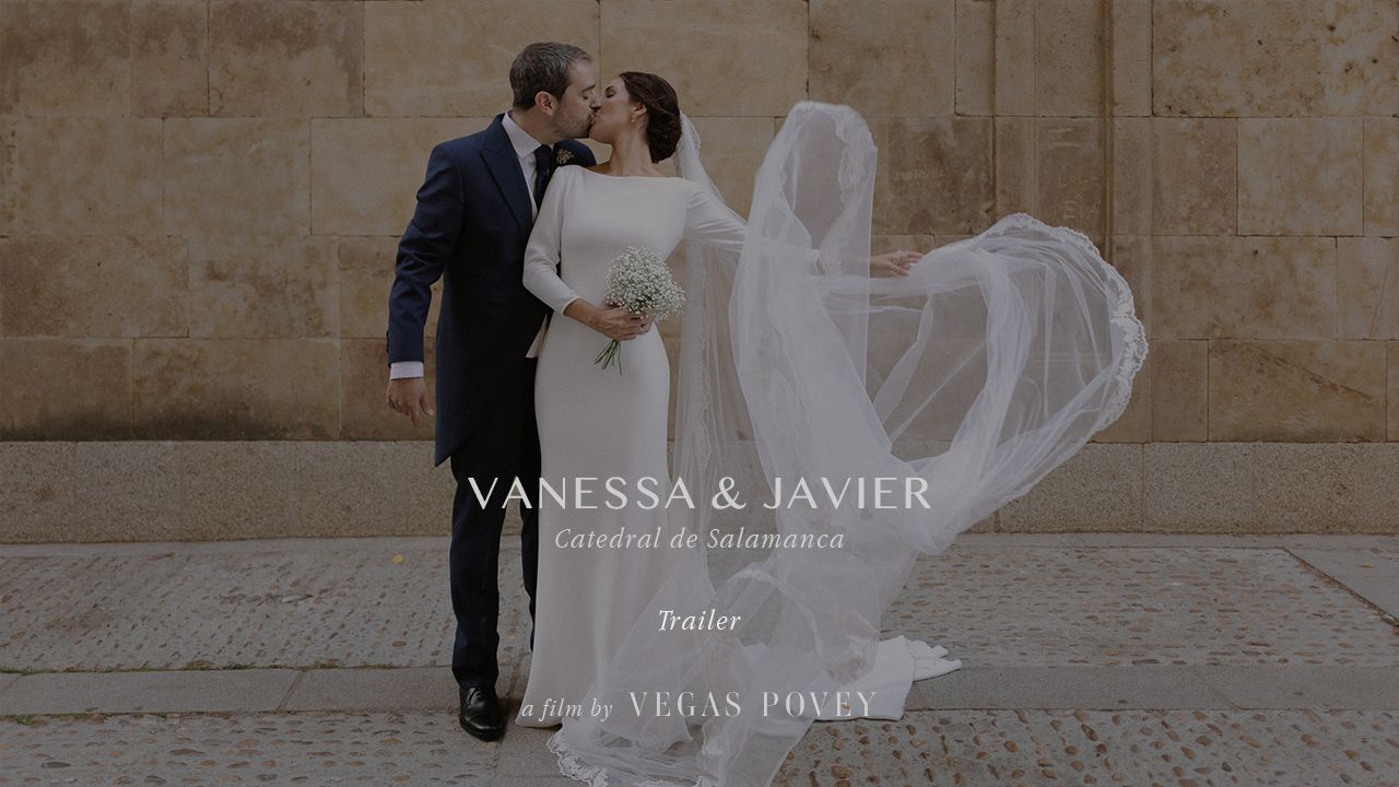 A romantic wedding moment captured as a veil floats in the breeze against a stone wall backdrop.