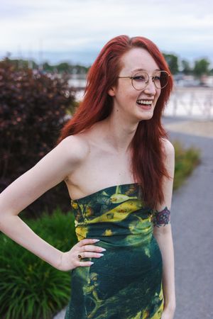 A woman in a green floral dress poses outdoors with a joyful expression.