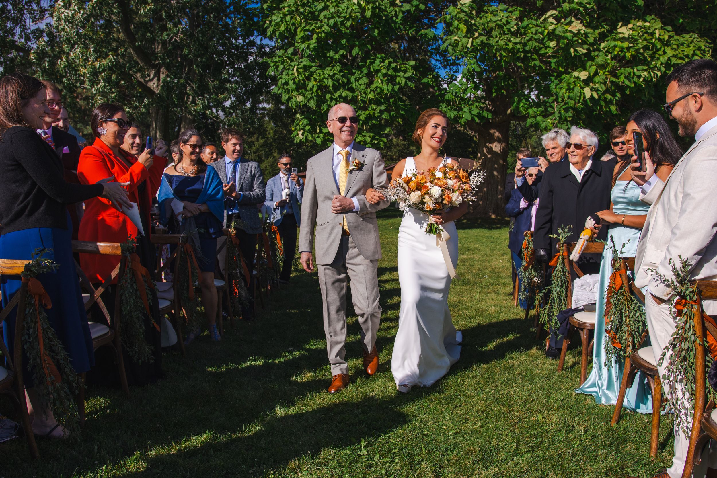 A group of wedding guests gather outdoors in a garden setting during a summer celebration.