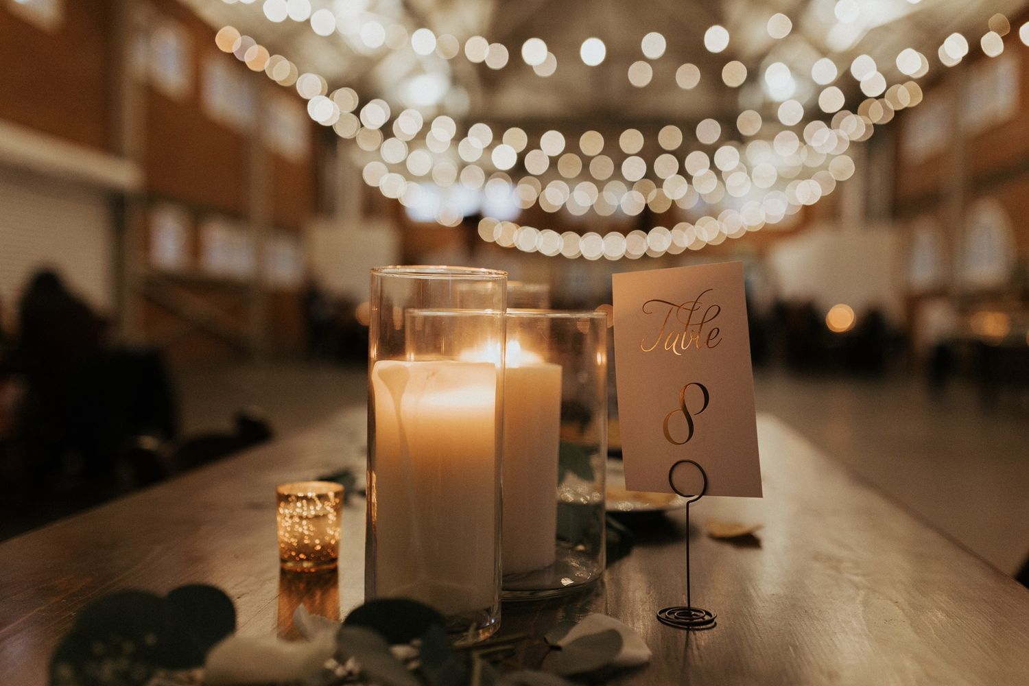 Lit candles and table numbers create an intimate ambiance under string lights at a wedding reception.