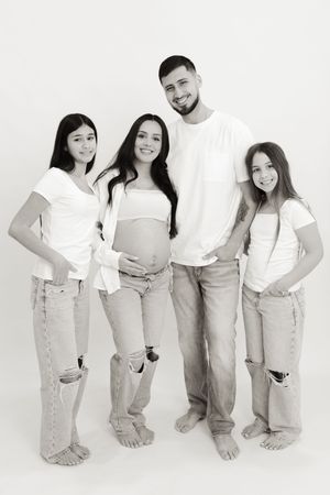 A family group poses together in coordinated white tops and light denim for a studio portrait.