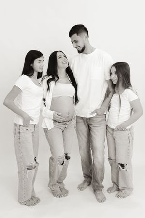 Family maternity photo with everyone wearing matching white tops and light denim.