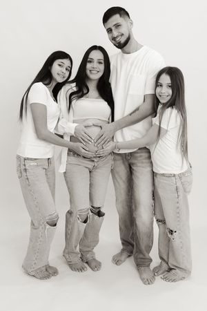 Family maternity photo series showing group in coordinated white tops and jeans against white backdrop.