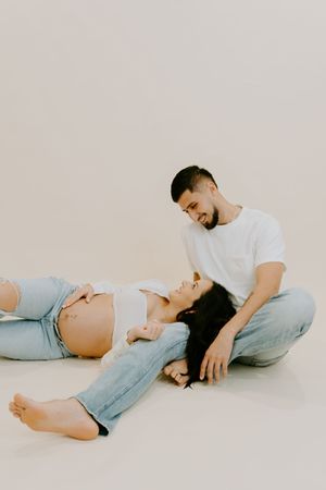 Artistic maternity photos showing couple in casual wear lying down during intimate photoshoot.