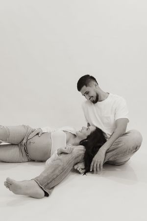 A black and white maternity photo of a couple sharing a tender moment while lying on the floor.
