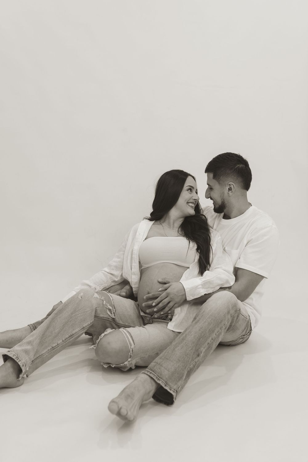 Artistic black and white maternity photos showing a couple laying together on the floor in casual clothing.