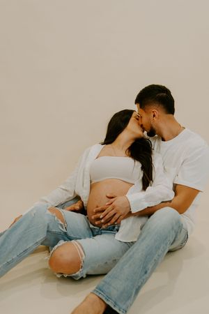 A couple in white shirts and jeans embrace intimately on the floor during a photo session.