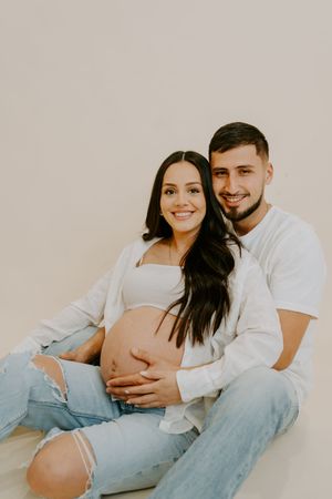 Expecting couple in matching denim and white outfits embrace during intimate maternity shoot.