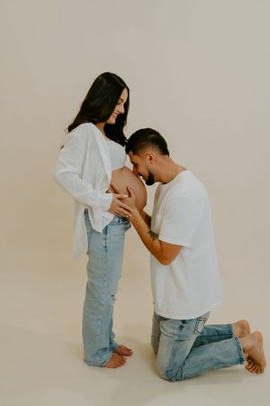 Tender moment between couple during pregnancy photoshoot on neutral background.