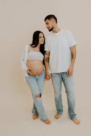 Artistic maternity photos of couple in matching white shirts and jeans against neutral background.