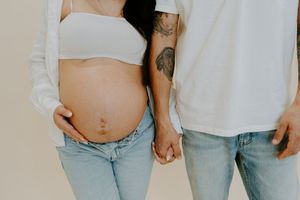 Couple wearing matching white t-shirts and light blue jeans hold hands while showing off a pregnancy bump.