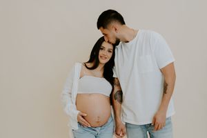 A couple in casual white tops and jeans pose together against a neutral background.