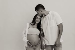 Black and white maternity photo of an expectant couple sharing an intimate moment against a plain backdrop.