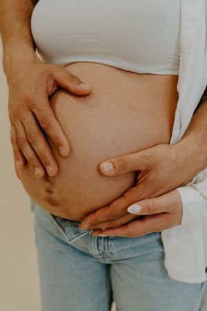 Close-up shots of hands tenderly cradling a pregnant belly in white top and light denim.