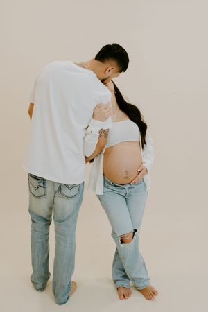 Candid maternity photography capturing tender moments between couple in matching casual outfits.