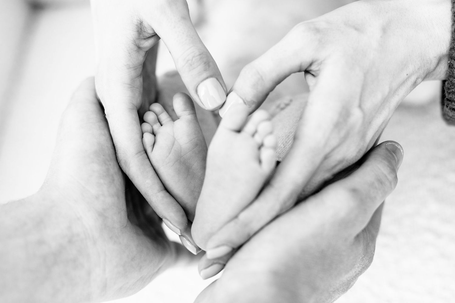 A series of black and white close-up photographs showing gentle hands holding and caressing a newborn baby.