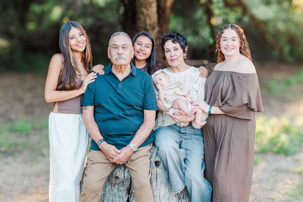 Family members pose together on rustic wooden benches during an outdoor portrait session in a garden.