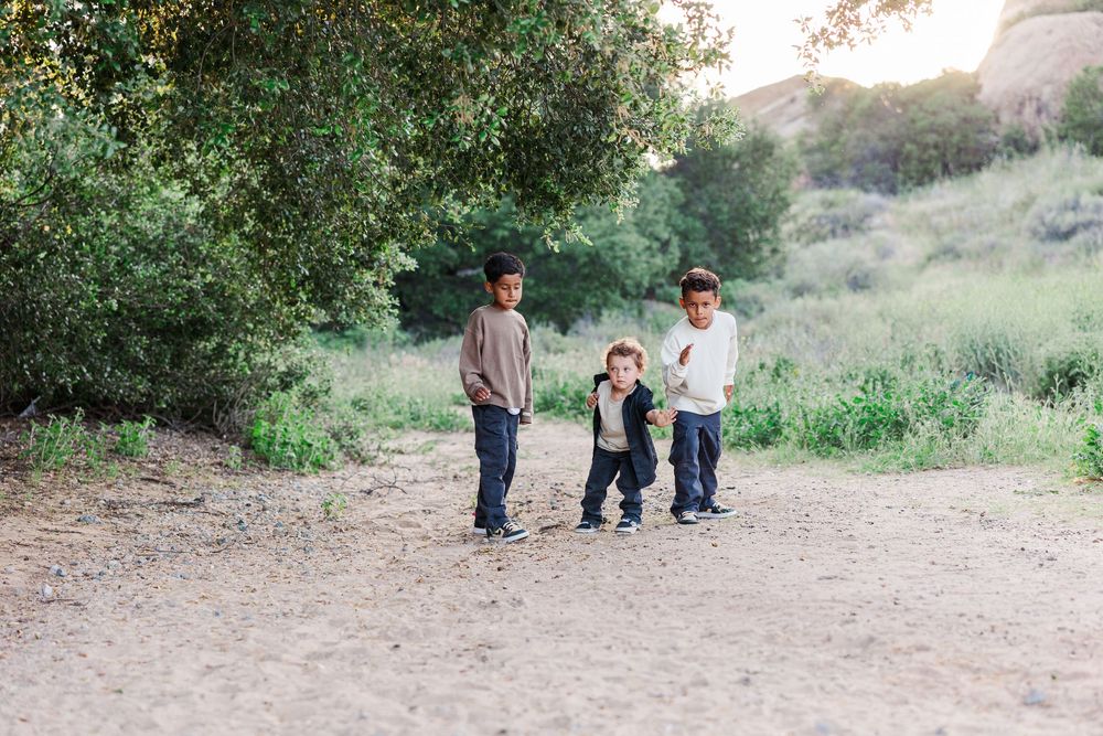 Family walking together on a dirt trail surrounded by green trees and natural landscape.