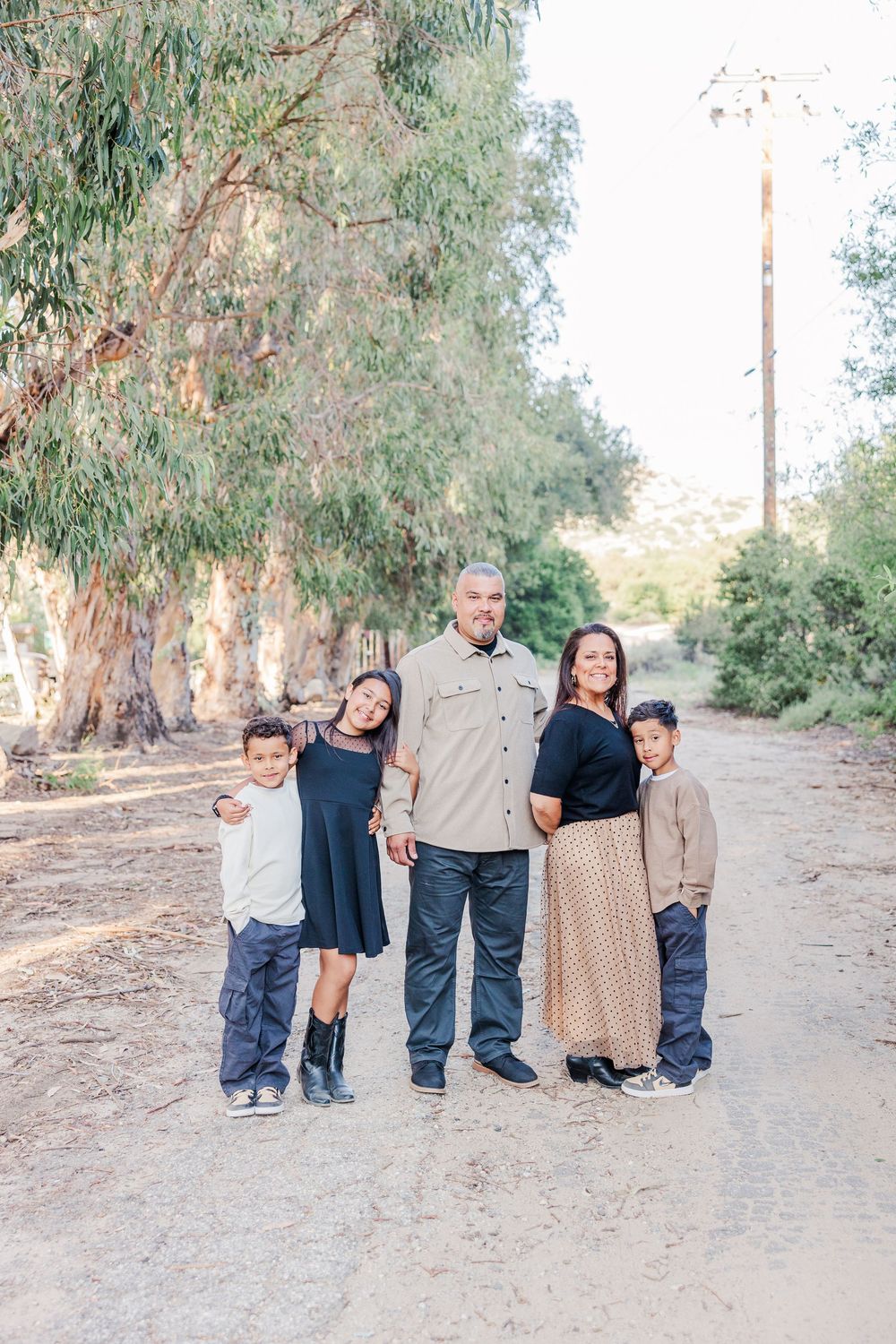 A family poses together for candid photos in a natural outdoor setting with eucalyptus trees.