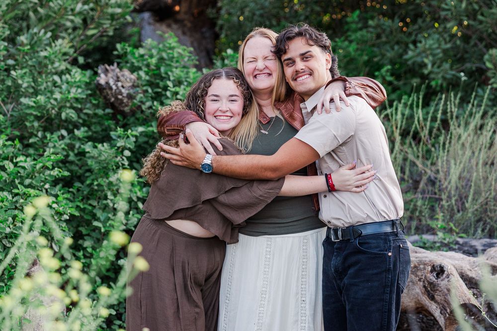 A group embraces and laughs together during an outdoor family photo session in a natural garden setting.