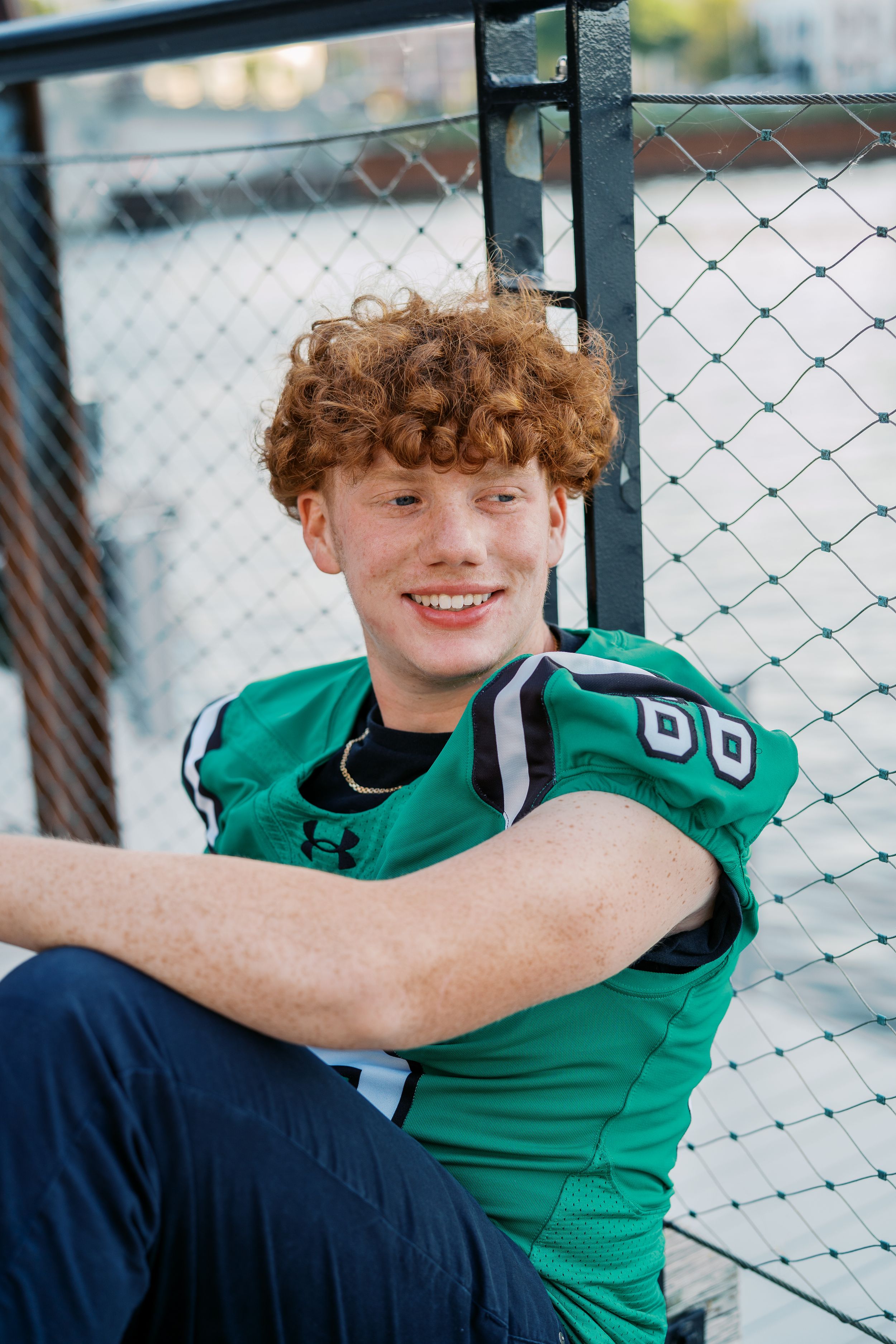 Athletic portrait featuring someone in a green jersey against a chain link fence.