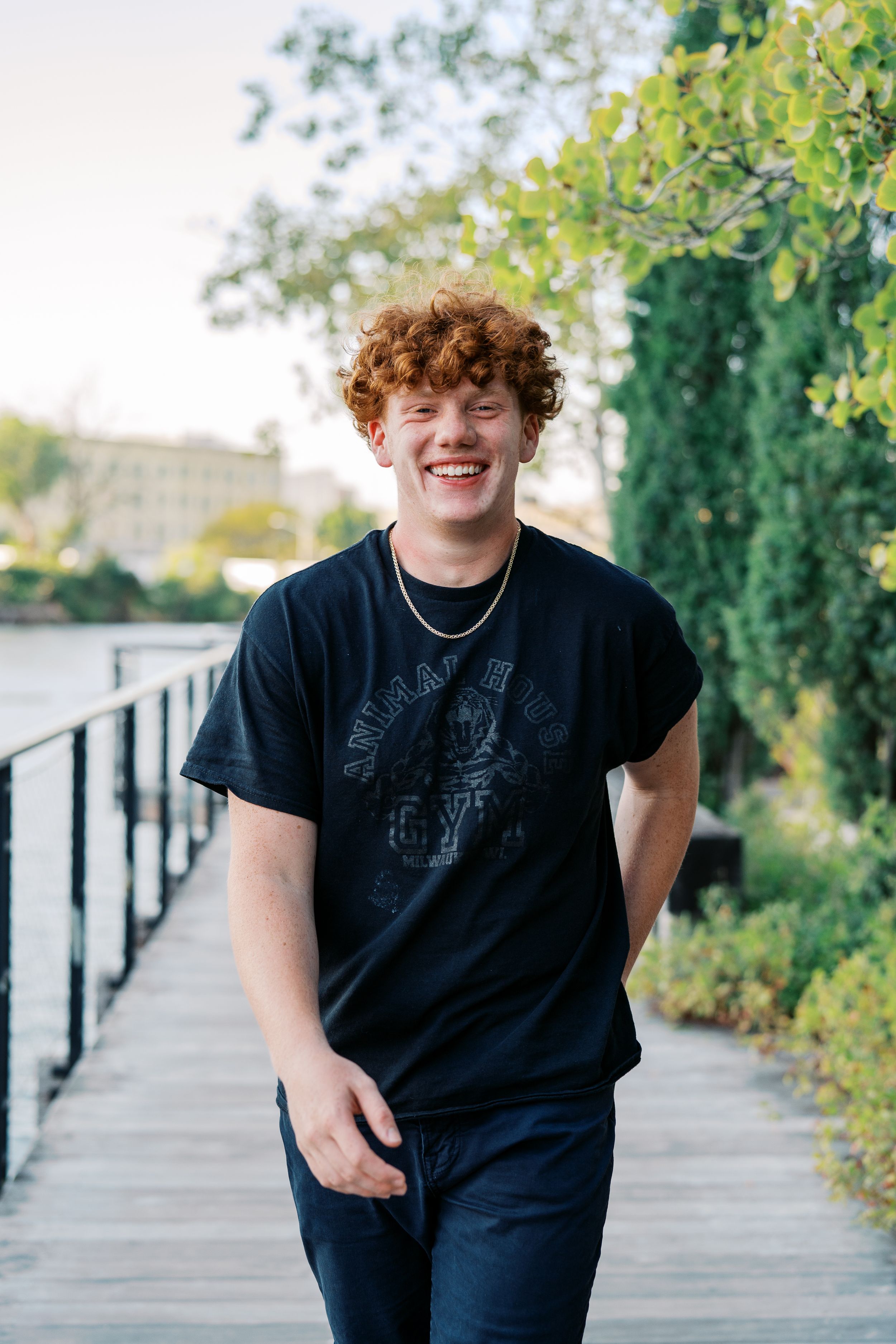 Outdoor portrait on walkway with lush greenery and architecture in background.