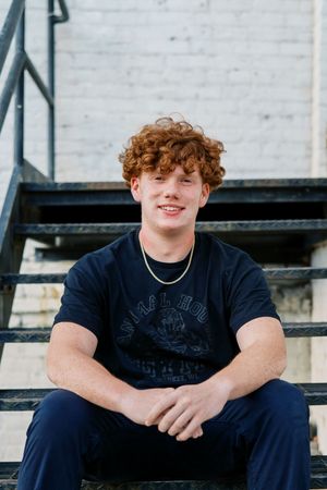 Portrait on metal stairs wearing dark graphic t-shirt and silver necklace.