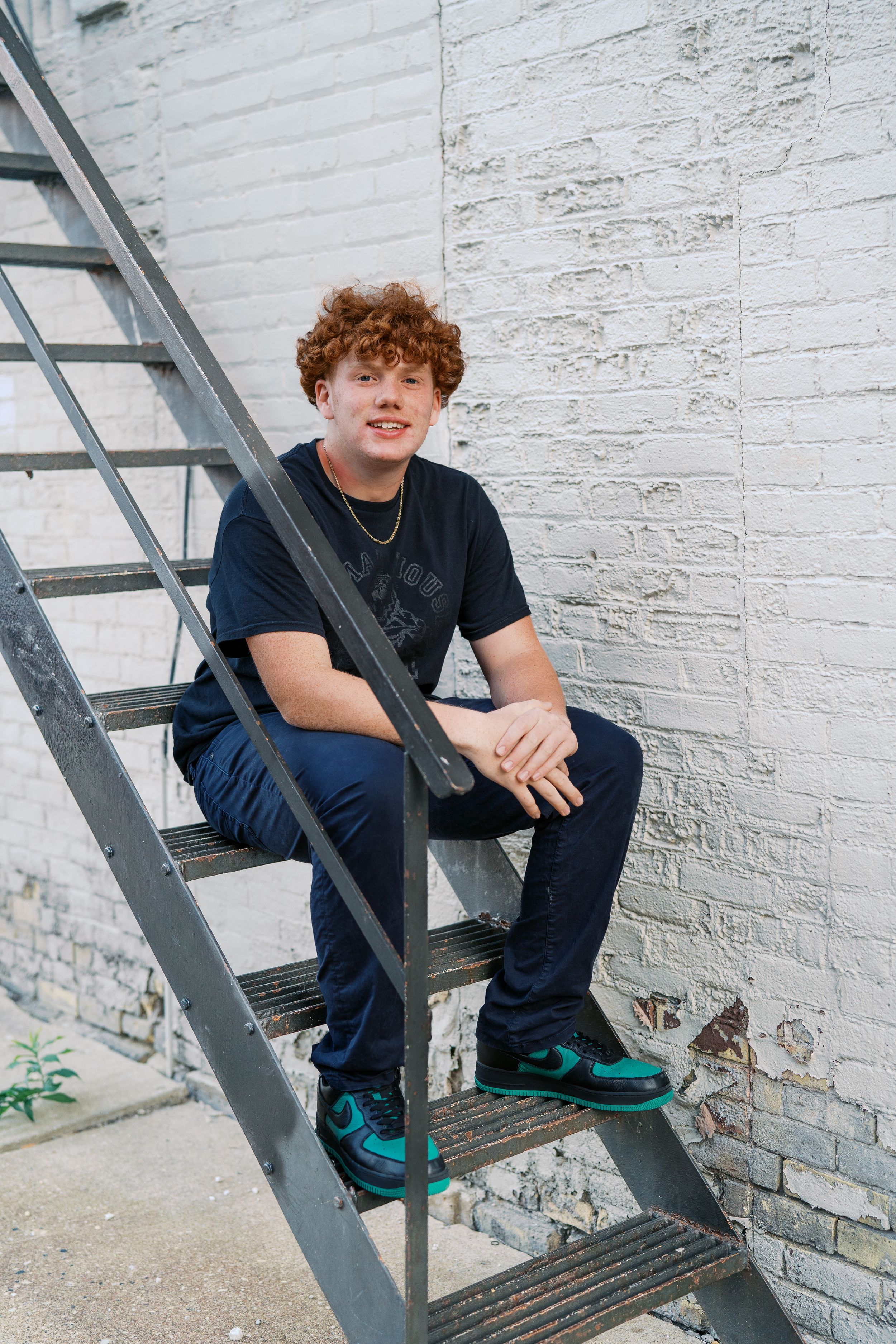 Casual portrait on metal fire escape stairs against white brick wall.