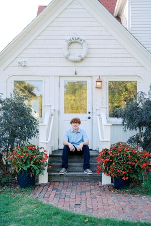 Person sitting on white porch steps with red flowers and life preserver decoration.