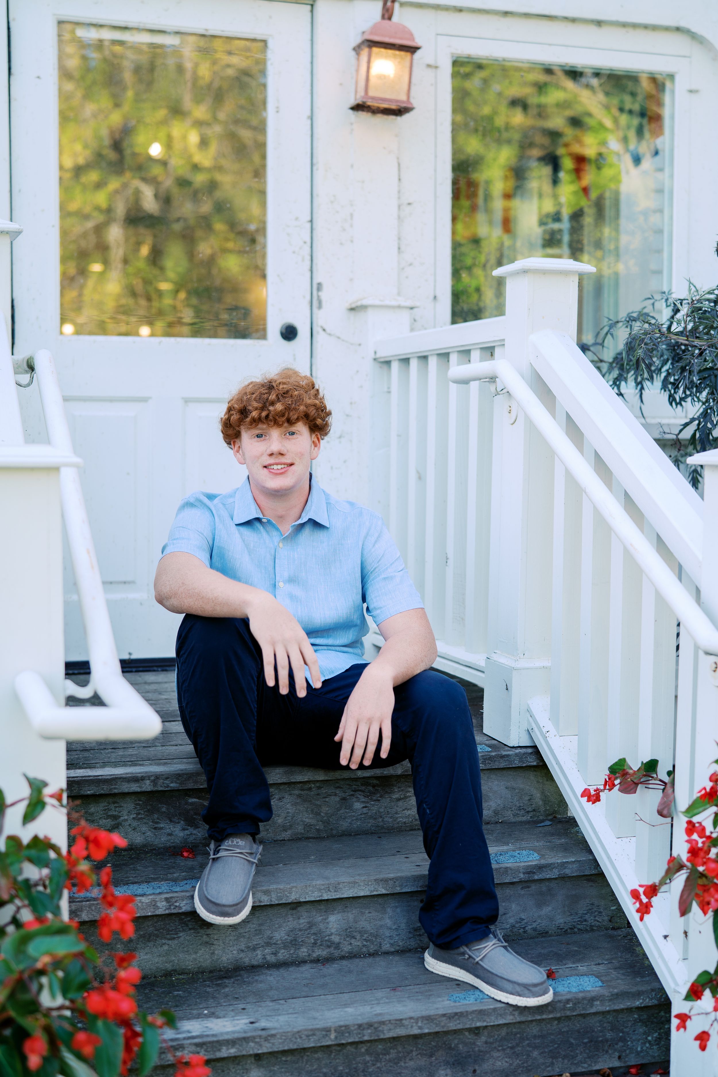Student sits casually on white porch steps with red flowers blooming nearby.