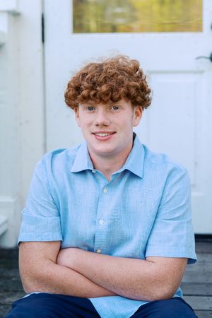 Student in light blue polo shirt poses against white porch railing.