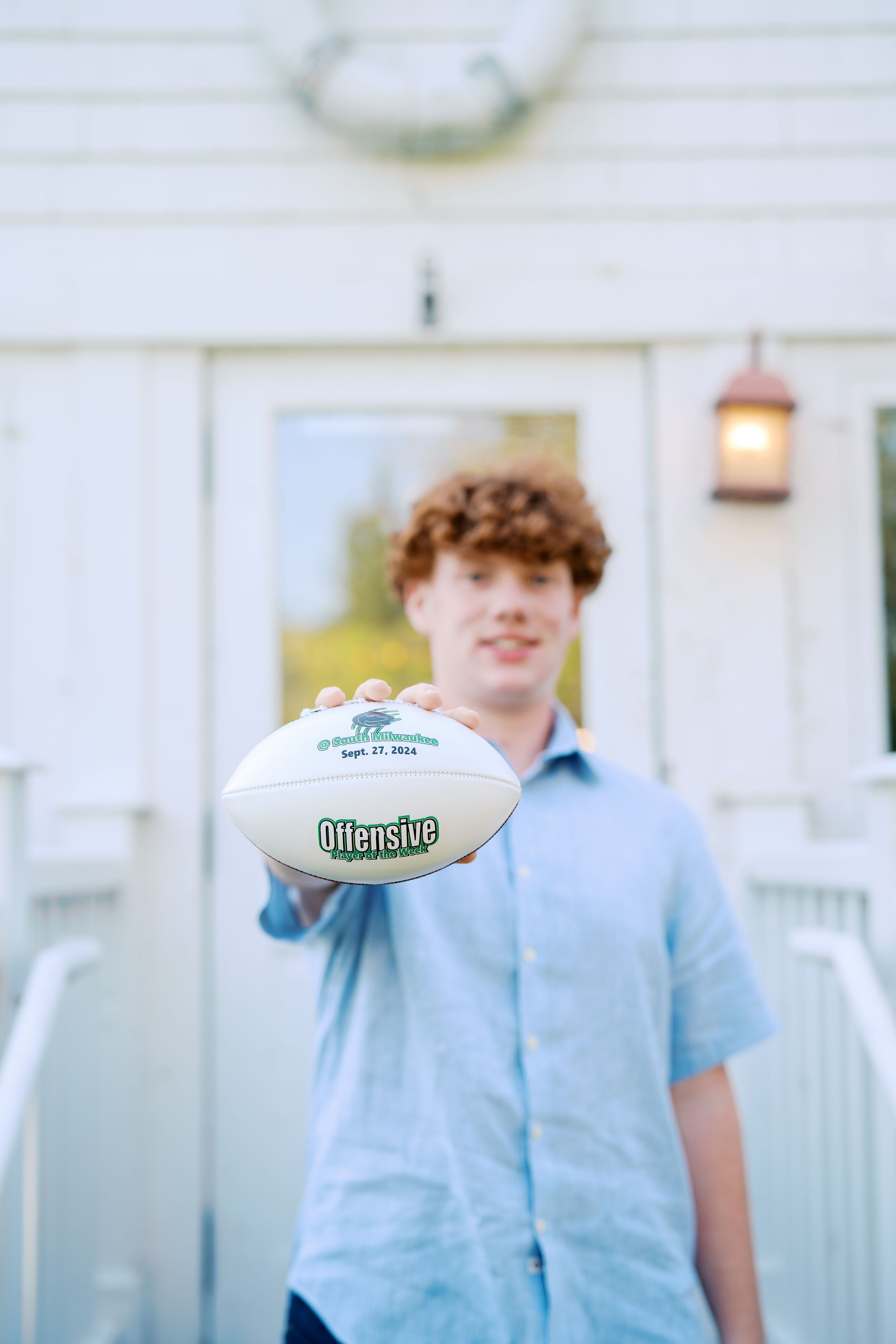 Student poses with a football on white porch in casual attire.