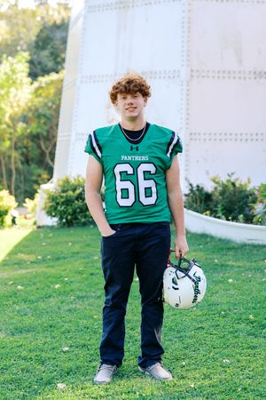 Football player wearing green Panthers jersey number 66 stands on grass field.