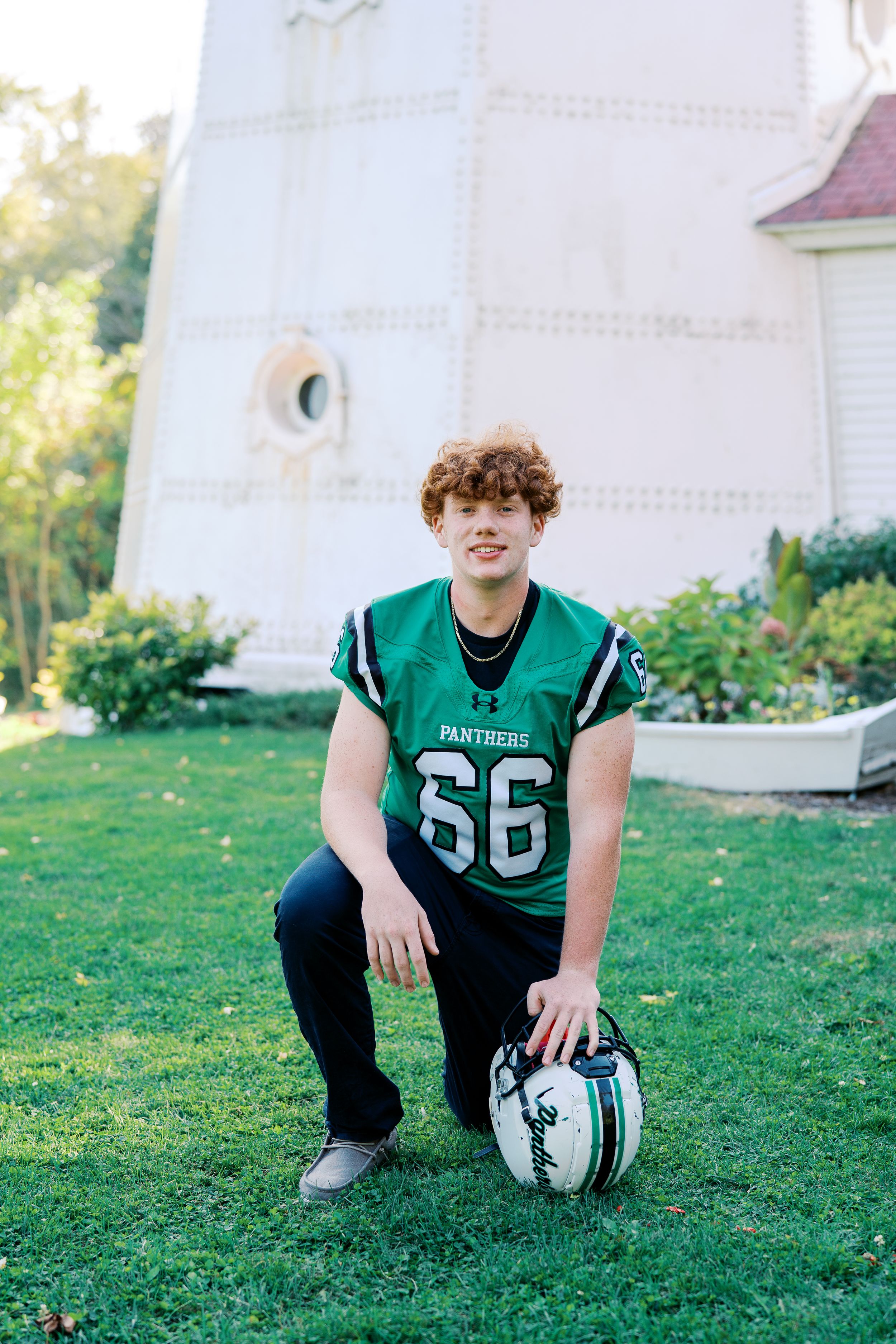 Panthers player in green jersey kneels with football on grass field.