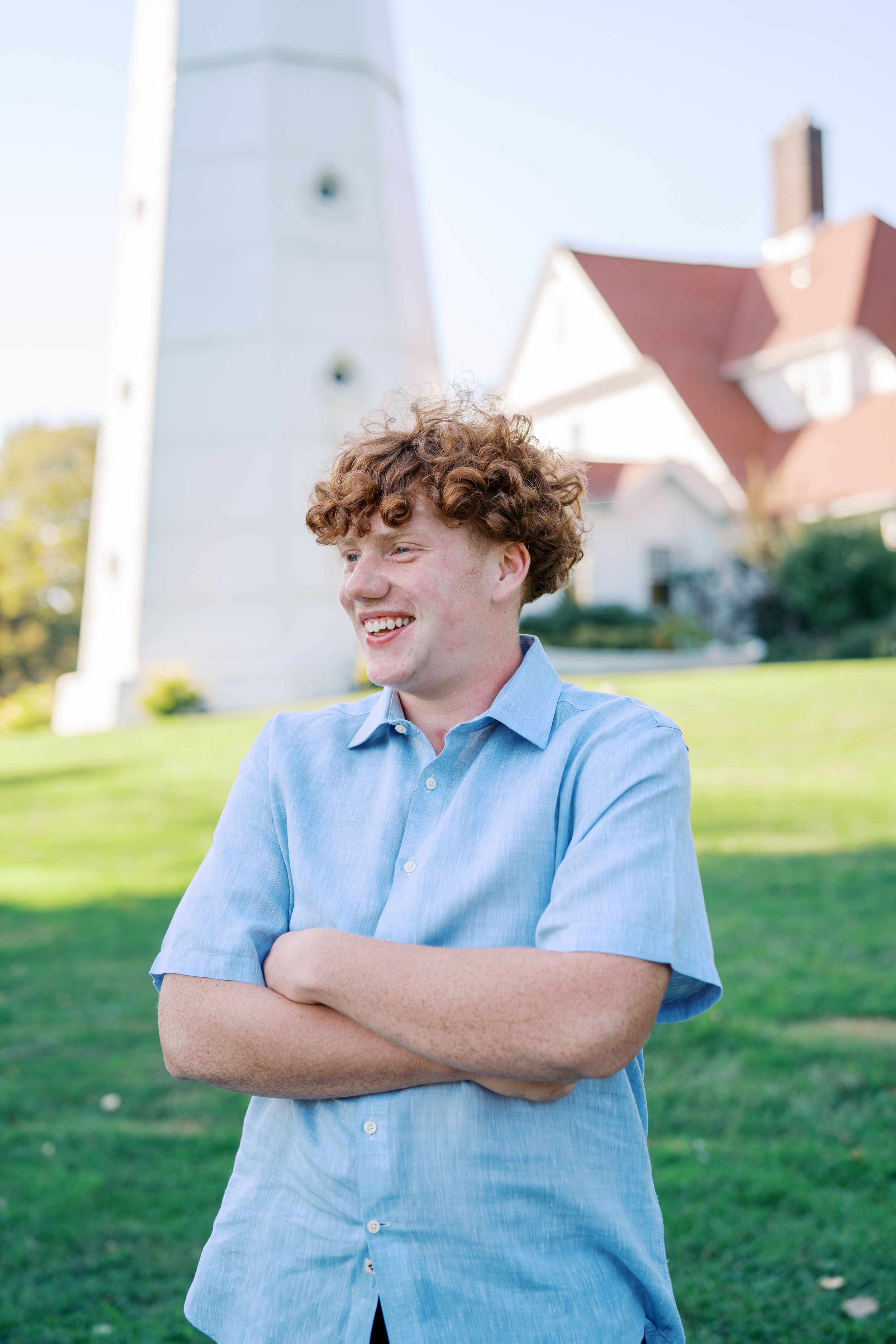 Person in light blue shirt smiling with lighthouse and pink building in background.
