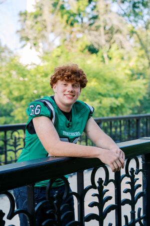 Football player in Panthers jersey leans against black railing outdoors.