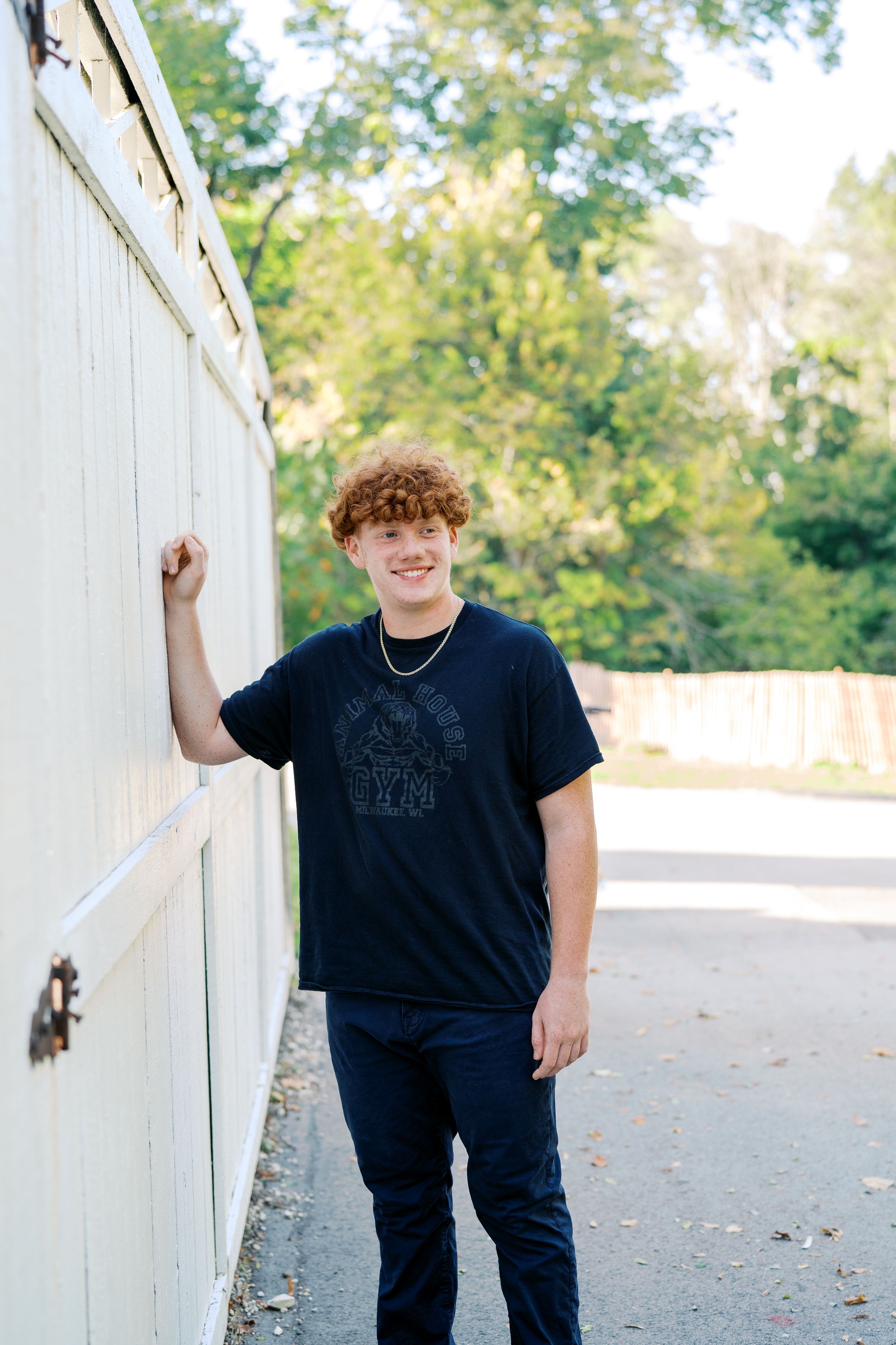 Student in black t-shirt poses against white outdoor wall.
