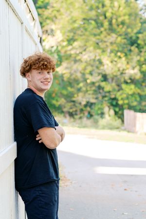 Student in dark clothing poses casually against white wall outdoors.