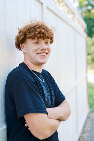 Student in black t-shirt smiles while posing against white wall.