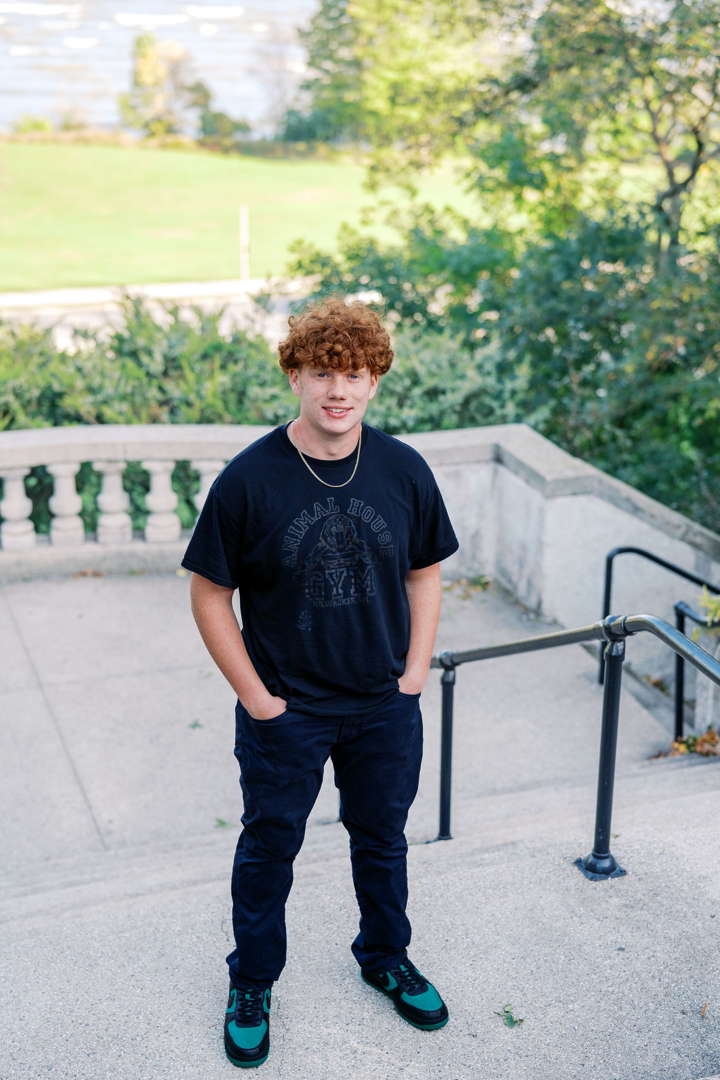 Casual outdoor portrait on stone steps with greenery and railing in background.
