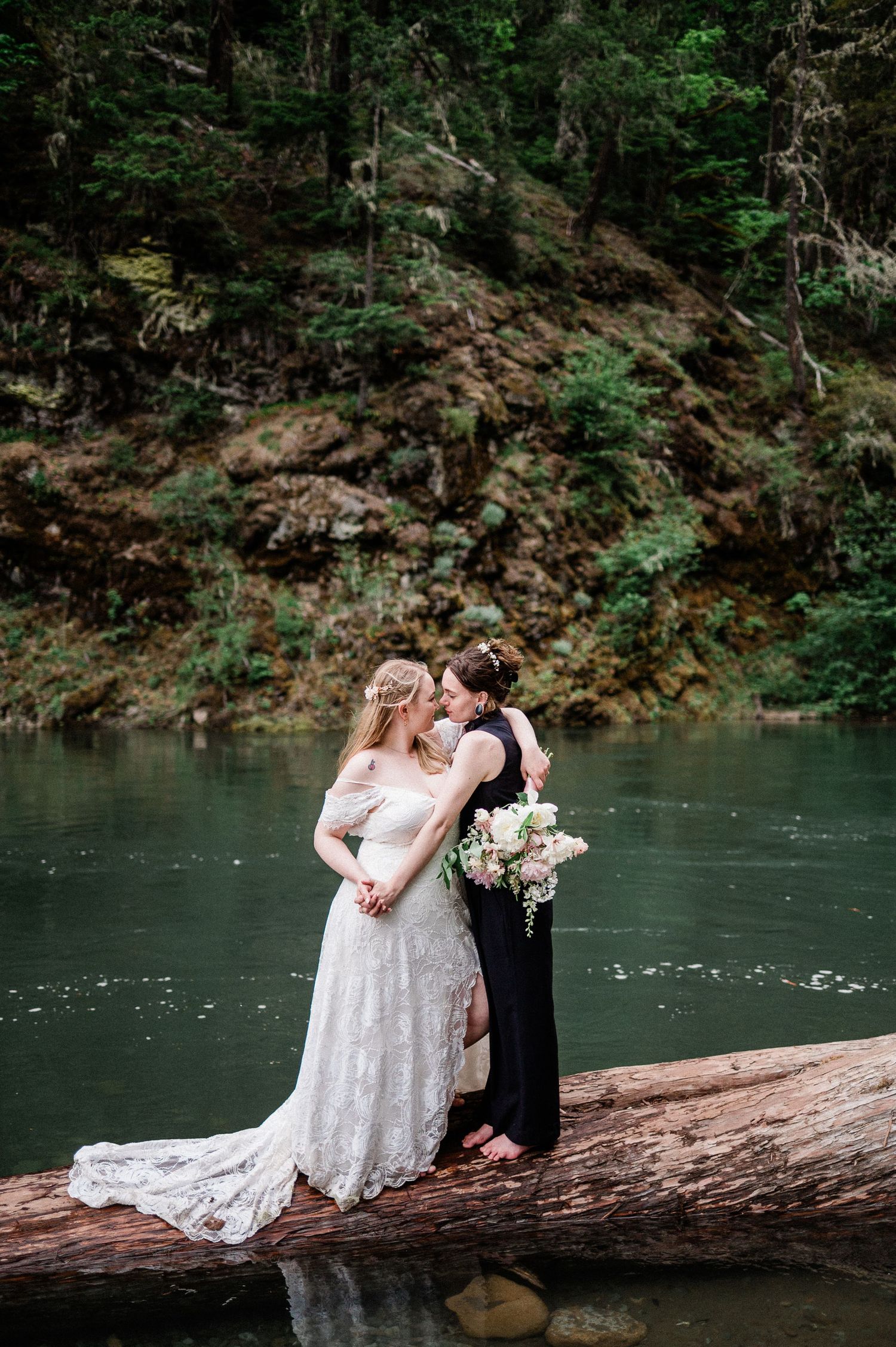 A couple shares an intimate moment on a fallen log over a serene turquoise river