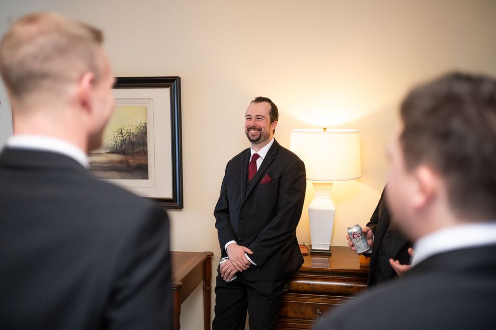 Men in formal attire gather in a room for pre-wedding preparations.
