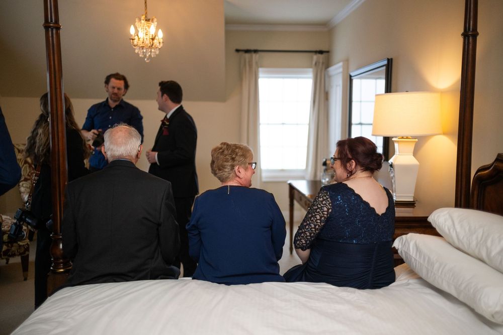 A dimly lit room with people seated in chairs facing towards a window with natural light streaming in.