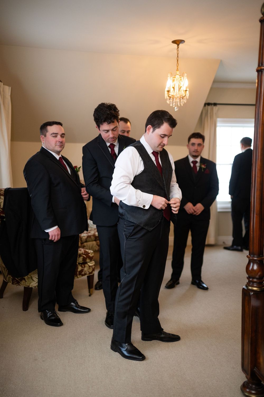Groomsmen in black suits and dress shoes getting ready in a room with a chandelier.